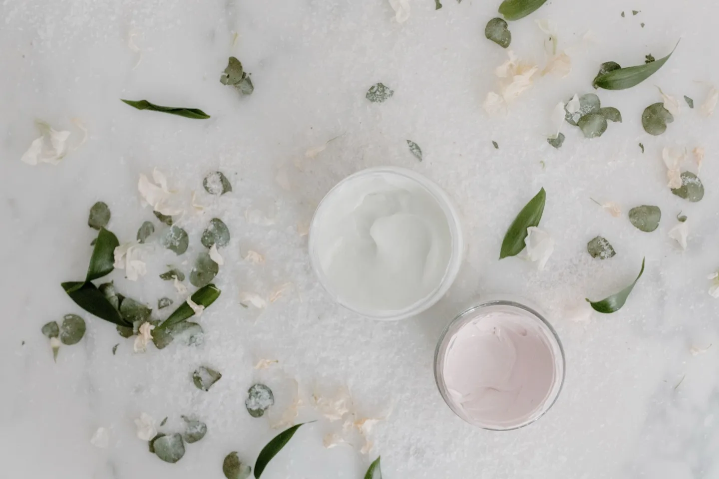 Deux pots de crème cosmétique posés sur un fond de feuillage et de pétales